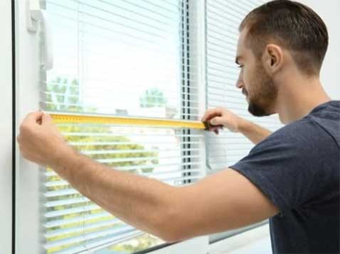 A man holding up a measuring tape to a window